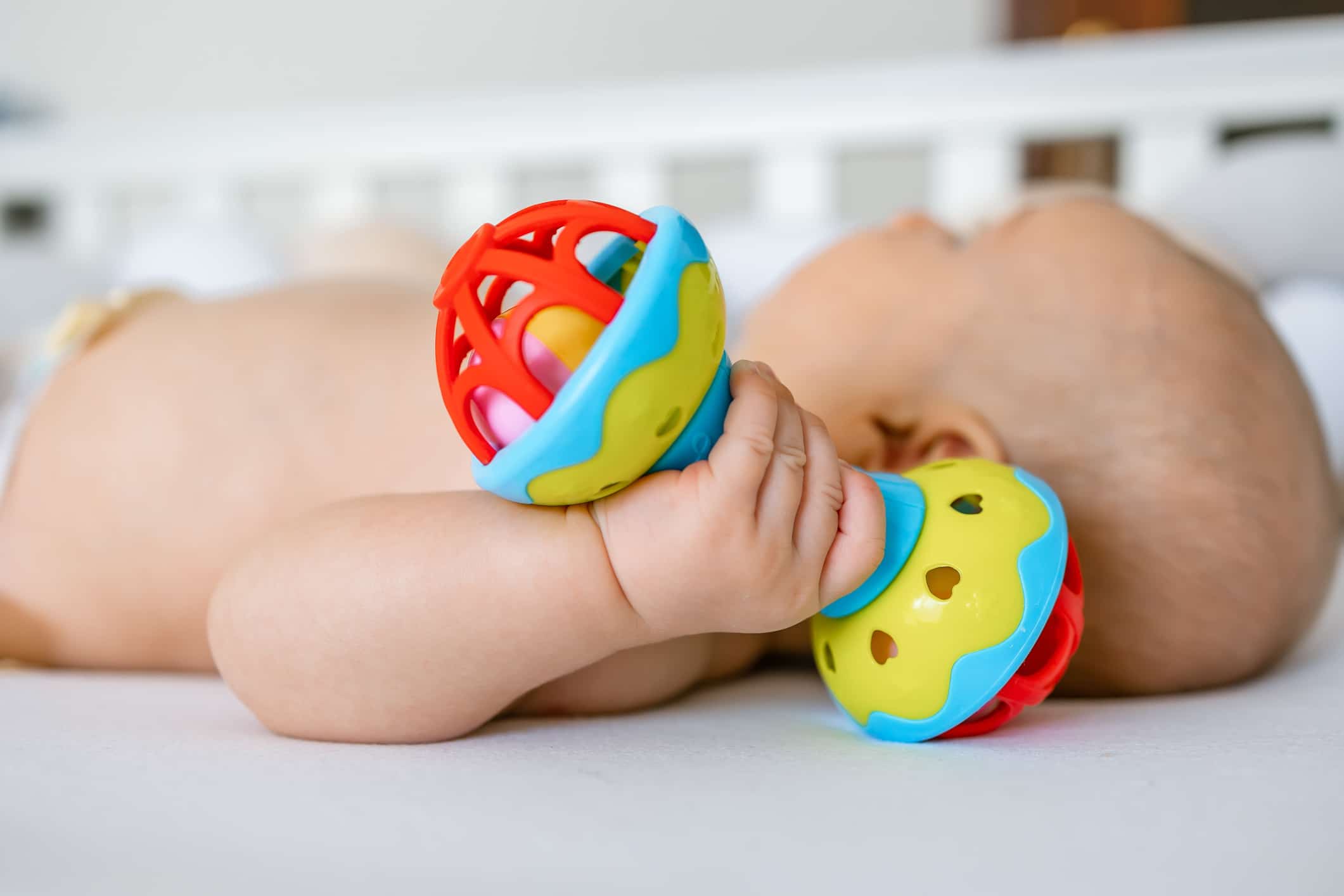 baby is lying at home on the bed , holding a rattle toy